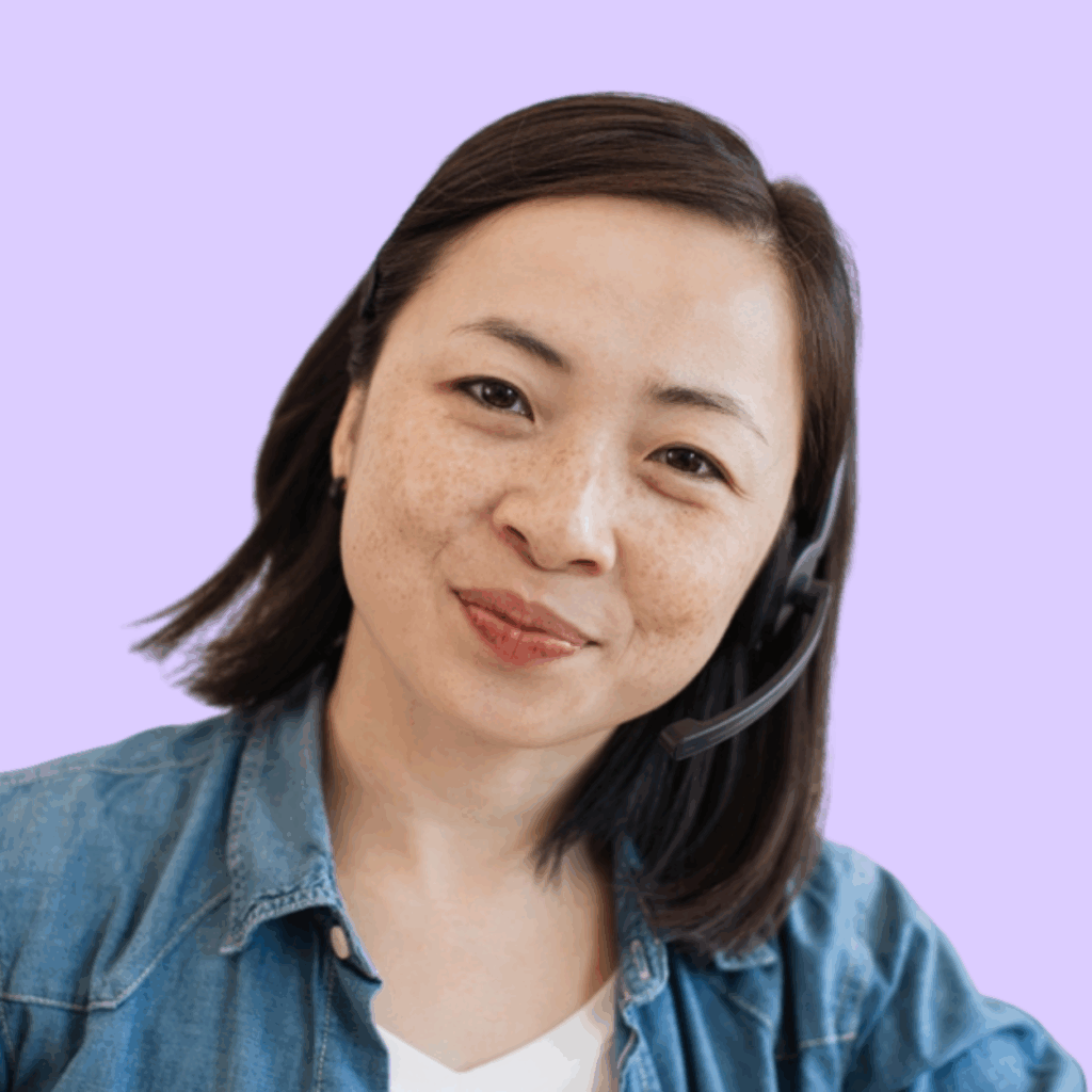 A woman wearing a denim shirt and a headset smiles gently at the camera, set against a light purple background.